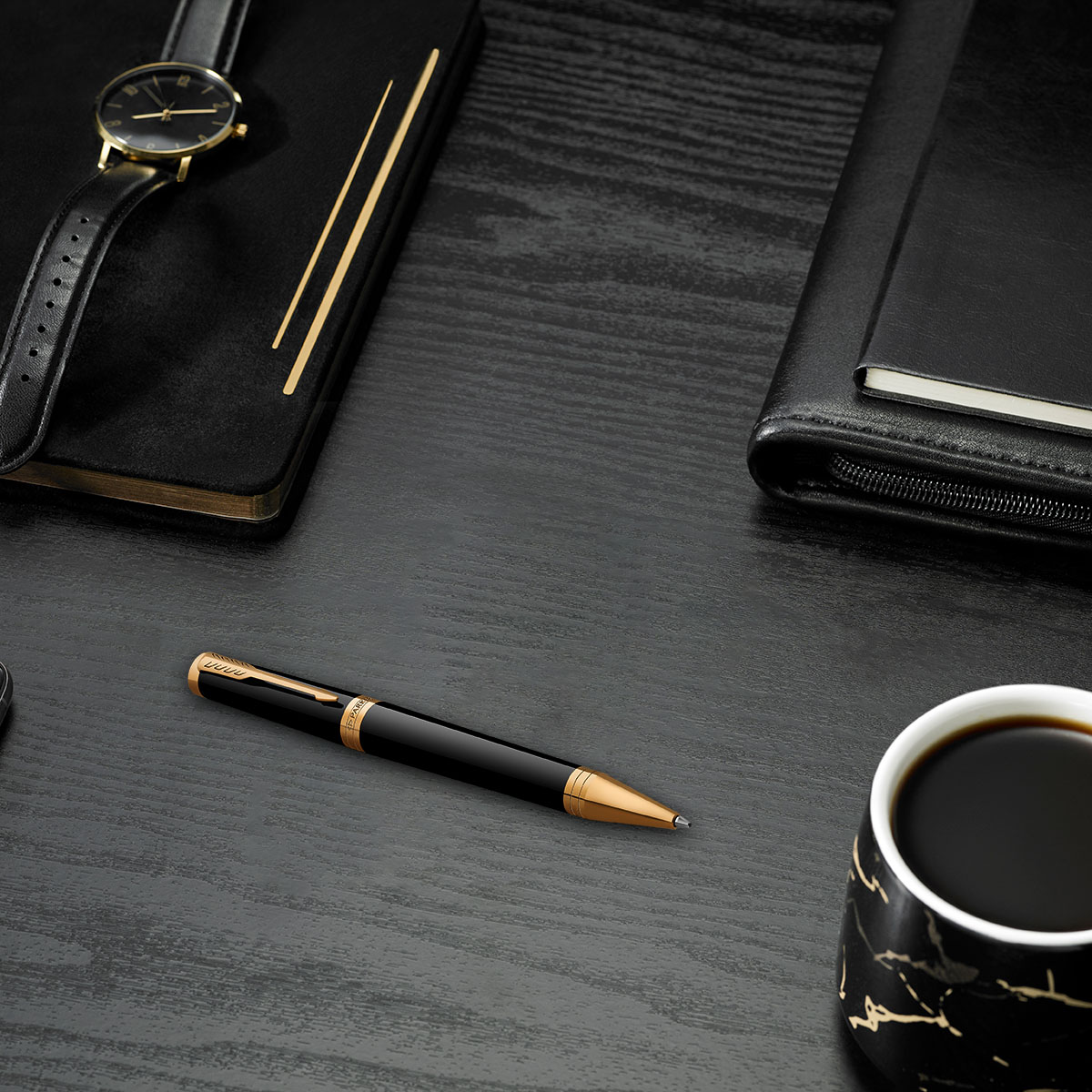 Czarny długopis z złotymi wykończeniami na eleganckim biurku obok notesu, zegarka i filiżanki kawy.